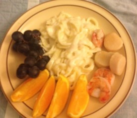 Fettuccine Alfredo, prawns, and scallops with orange slices and grapes